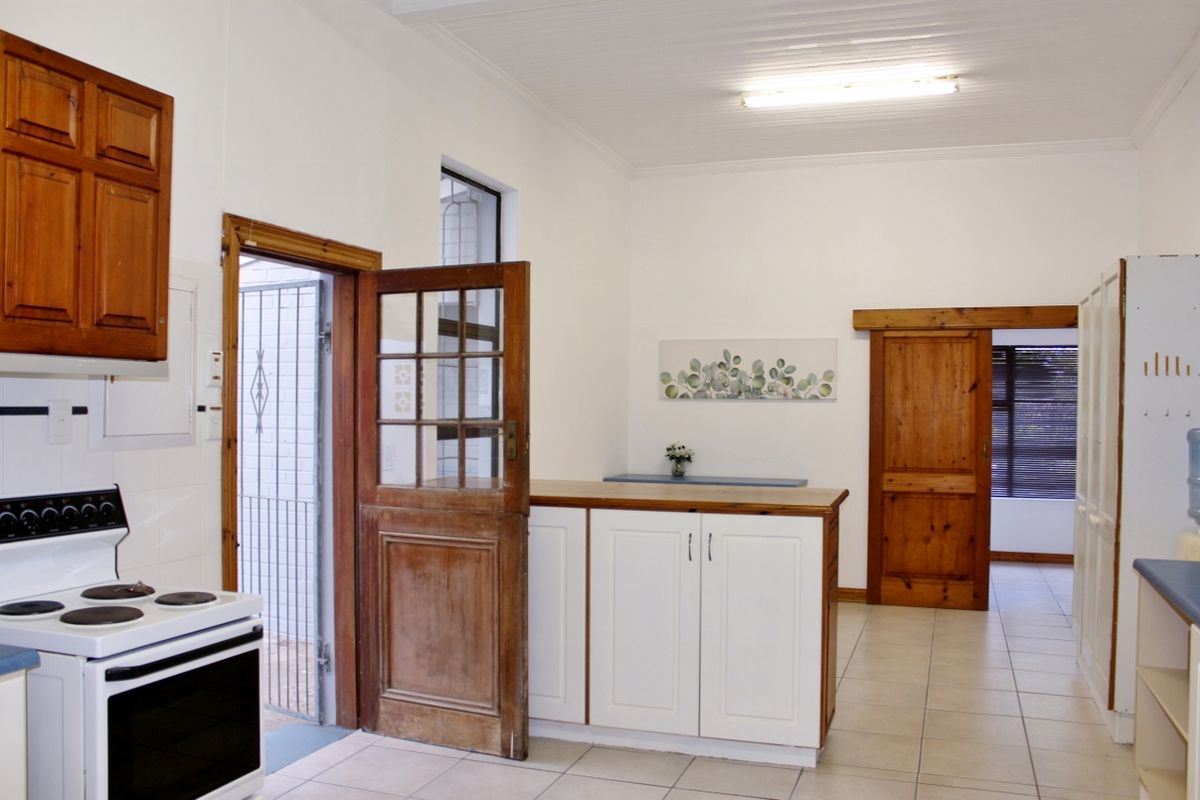 A functional kitchen featuring wooden cabinetry, tiled flooring, and a freestanding stove, with direct access to an outdoor area and adjacent room.