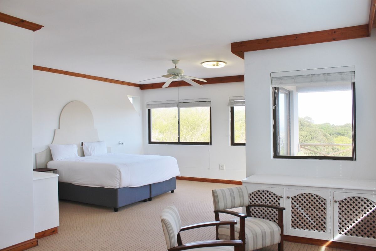 Spacious bedroom featuring neutral carpeting, timber ceiling accents, a ceiling fan, and built-in cabinetry with views of the surrounding greenery.