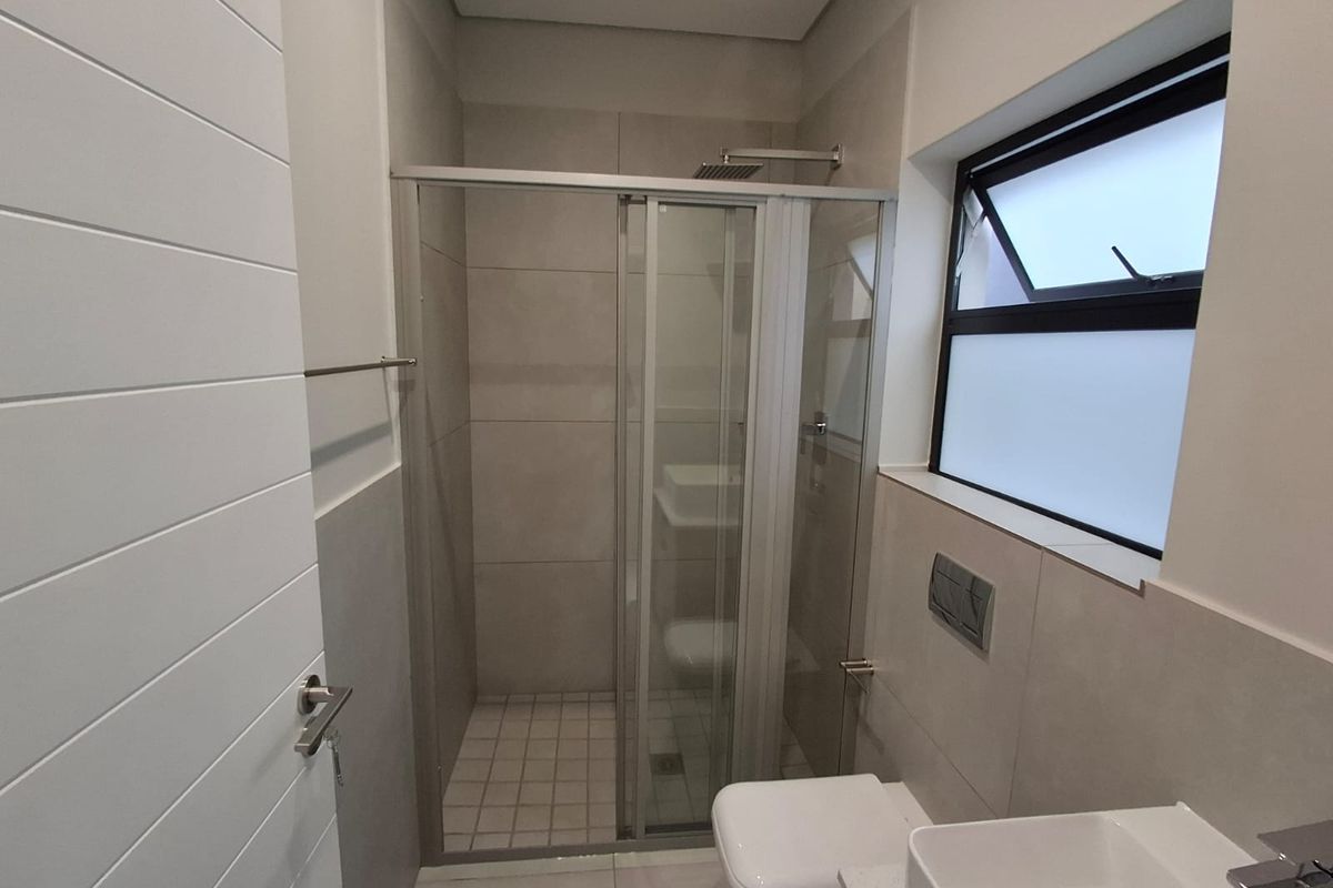 Modern bathroom featuring a glass-enclosed shower, wall-mounted toilet, and contemporary basin with neutral floor-to-ceiling tiling.