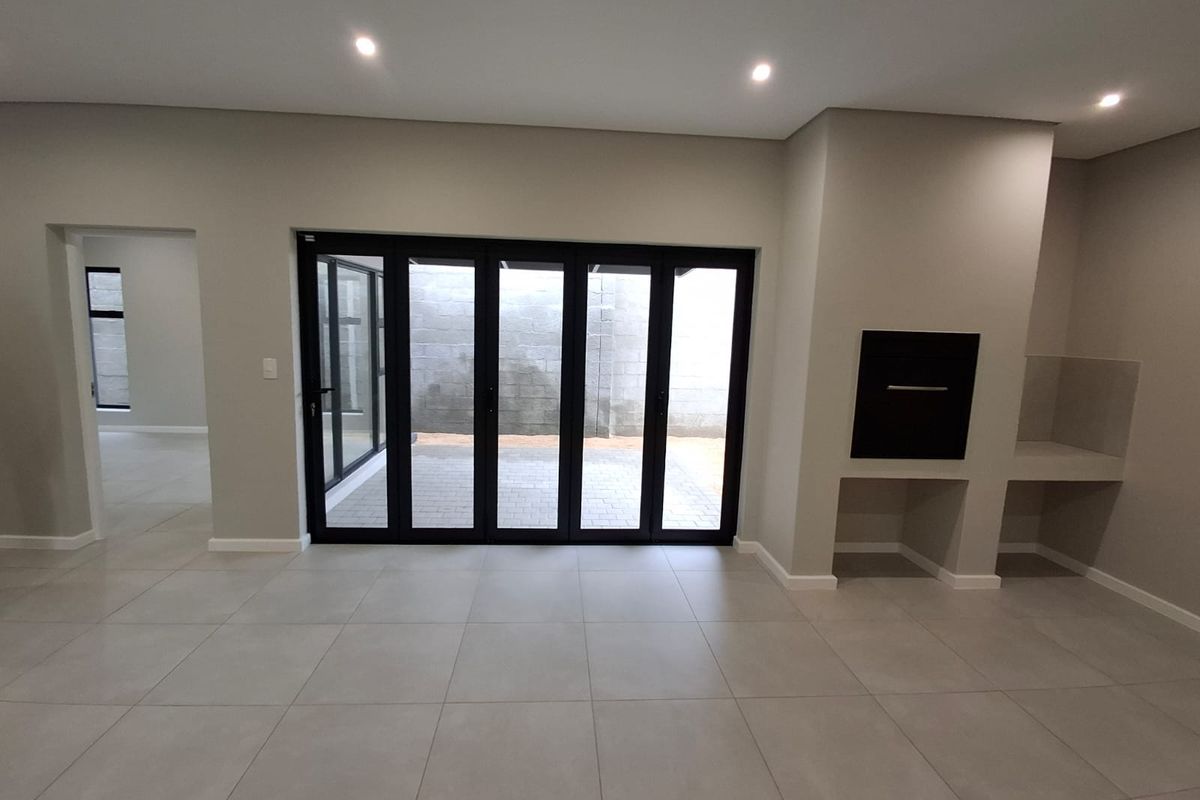 Spacious living area featuring large black-framed stacker doors leading to an outdoor patio, built-in fireplace, and neutral tiled flooring throughout.