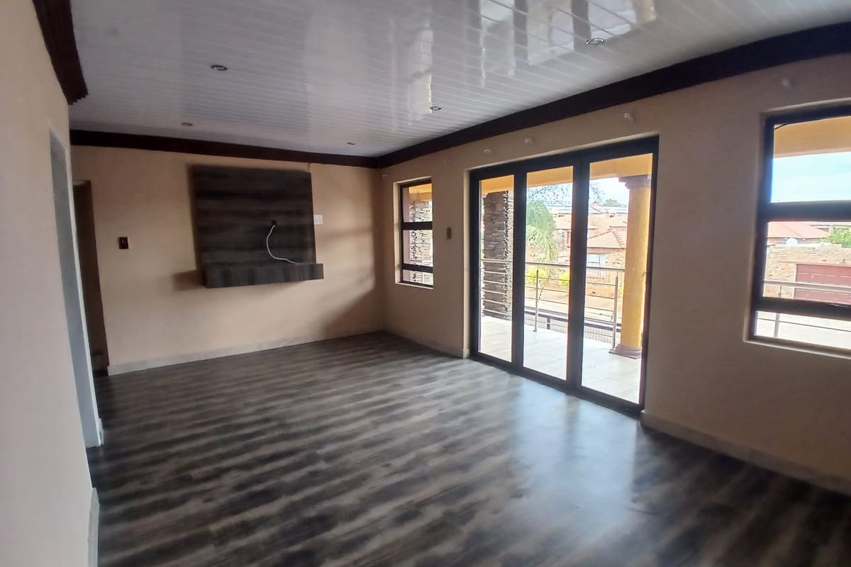 Spacious living room featuring modern laminate flooring, a sleek PVC ceiling with recessed lighting, and large sliding glass doors leading to an outdoor balcony.