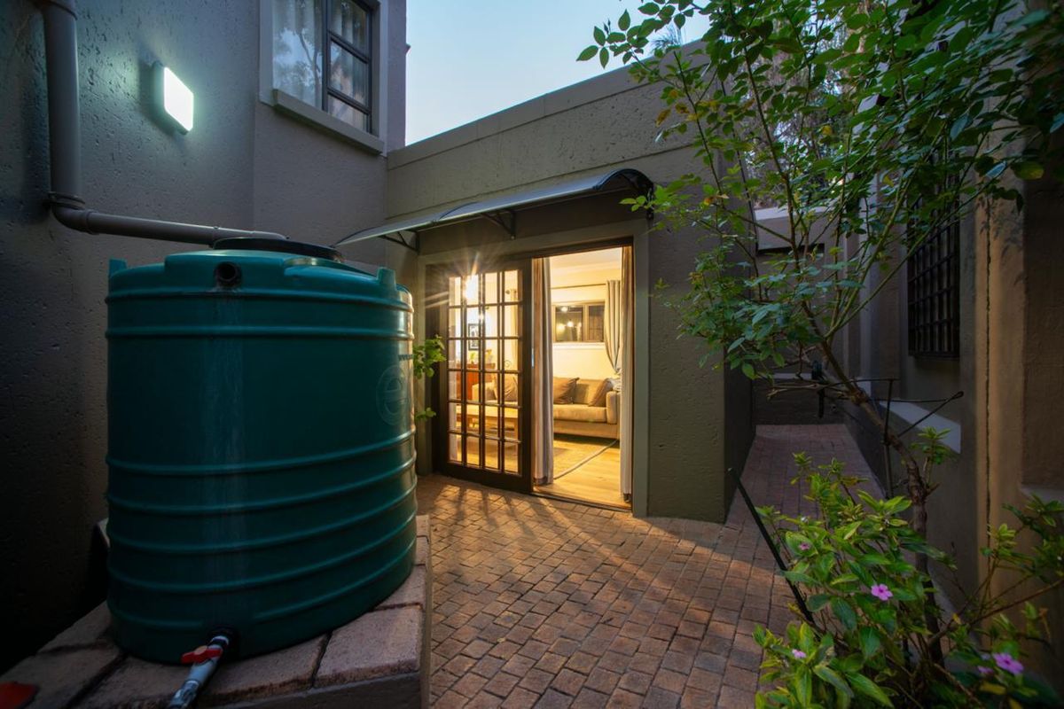 A private rear courtyard featuring paved flooring, a water storage tank, and direct access to the interior living space through a glass-paneled door.