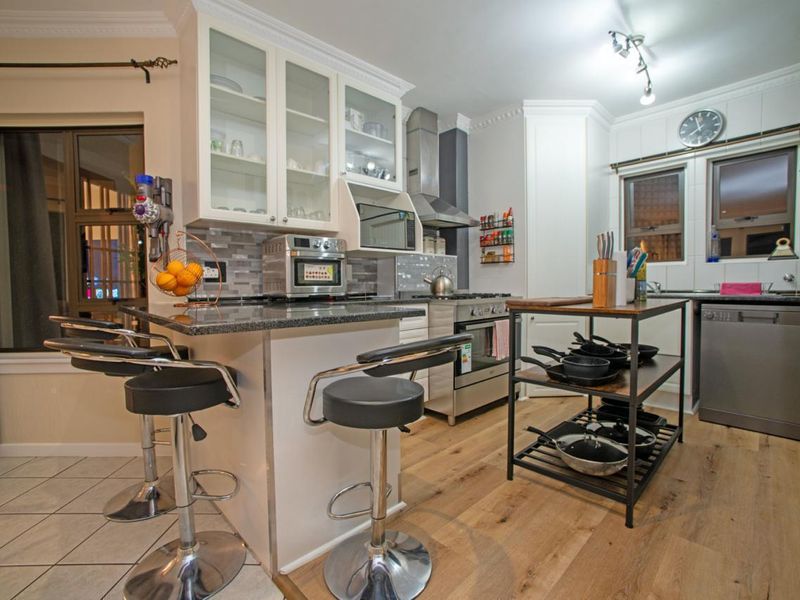 A well-appointed kitchen featuring granite countertops, glass-front cabinetry, a stainless steel extractor fan, and a breakfast nook with tiled and wood-look flooring.