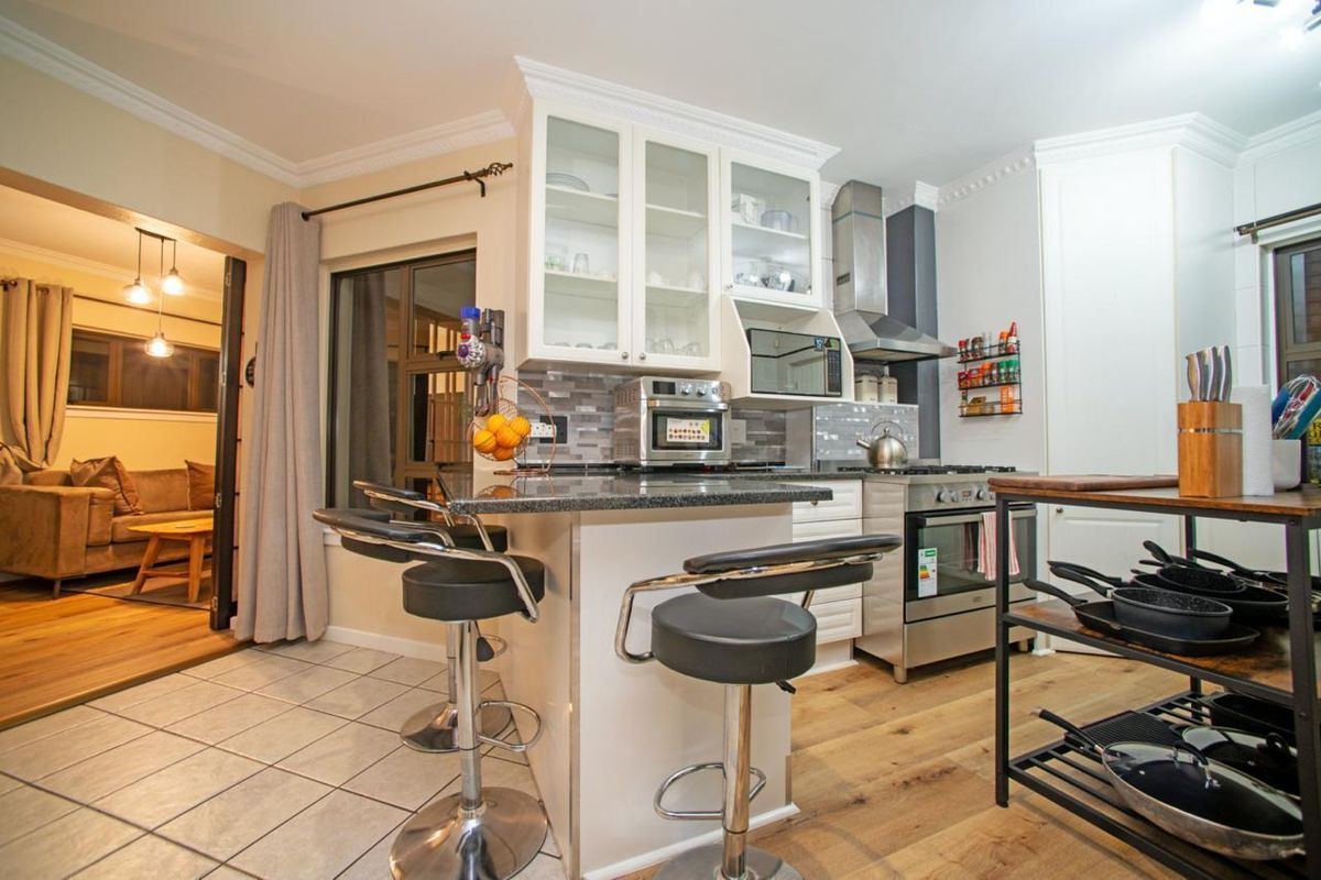 A well-appointed kitchen featuring granite countertops, glass-front cabinetry, a stainless steel extractor fan, and a gas stove, seamlessly flowing into the adjacent living area.
