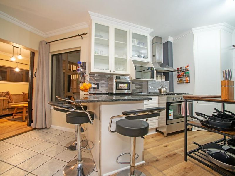 A well-appointed kitchen featuring granite countertops, glass-front cabinetry, a stainless steel extractor fan, and a gas stove, seamlessly flowing into the adjacent living area.