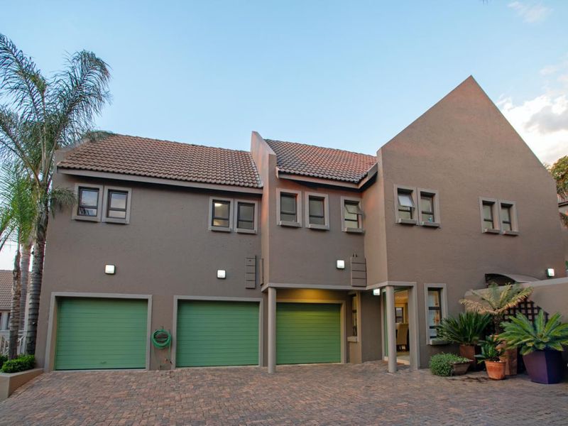 Front elevation of a multi-level cluster home featuring three green garage doors, paved driveway, and textured brown exterior walls.