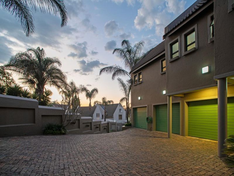 Exterior view of a cluster home featuring a paved driveway and multiple green garage doors at dusk.