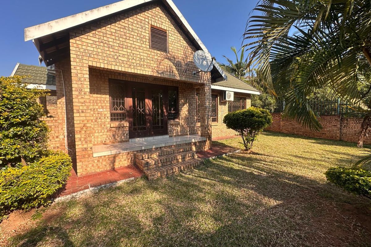 A rear view of a face brick house featuring a small patio area, established garden, and exterior security fixtures.