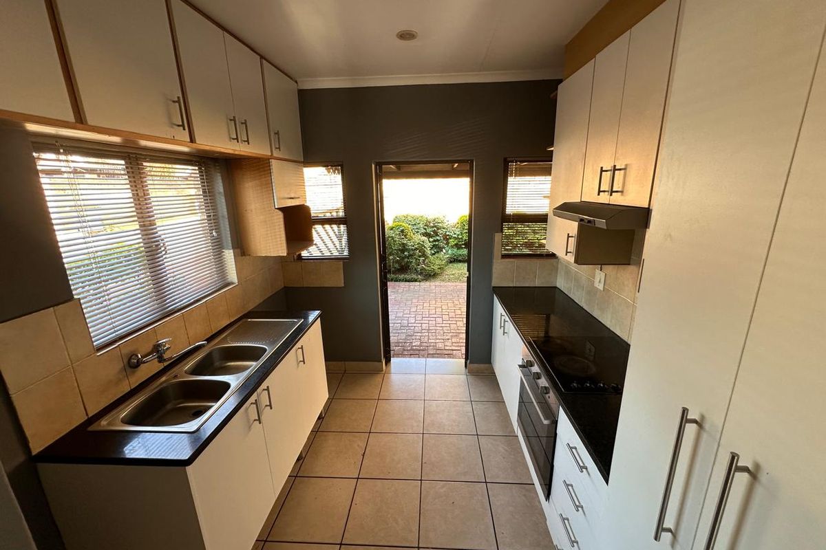 A functional galley-style kitchen featuring built-in cabinetry, a double sink, integrated oven and hob, and direct access to the rear garden.
