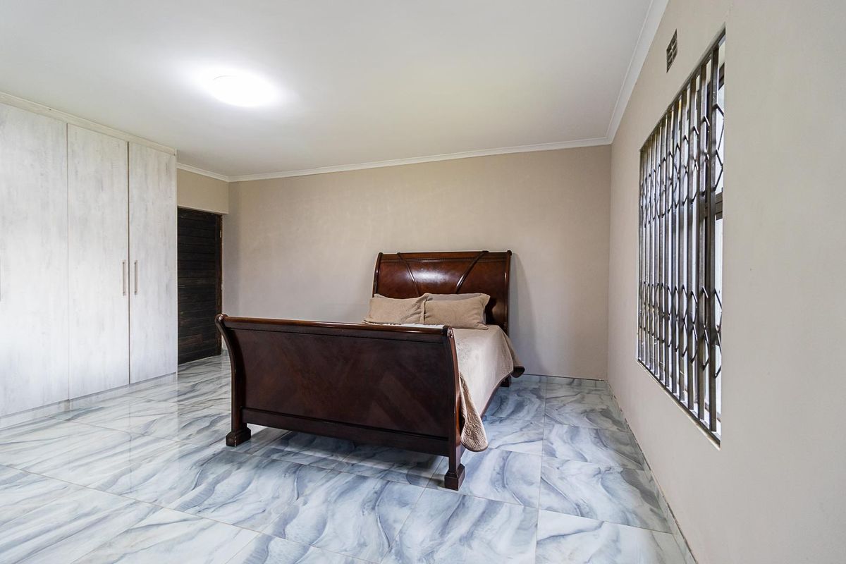 Spacious bedroom featuring modern tiled flooring, built-in cupboards, and a window fitted with a security gate.