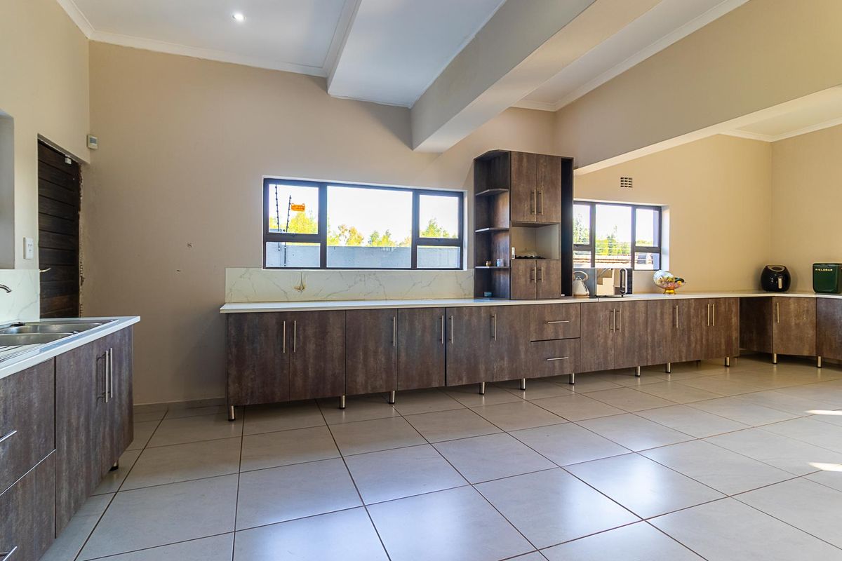 Spacious kitchen featuring modern wood-finish cabinetry, stone countertops, large tiled floors, and ample natural light through multiple windows.