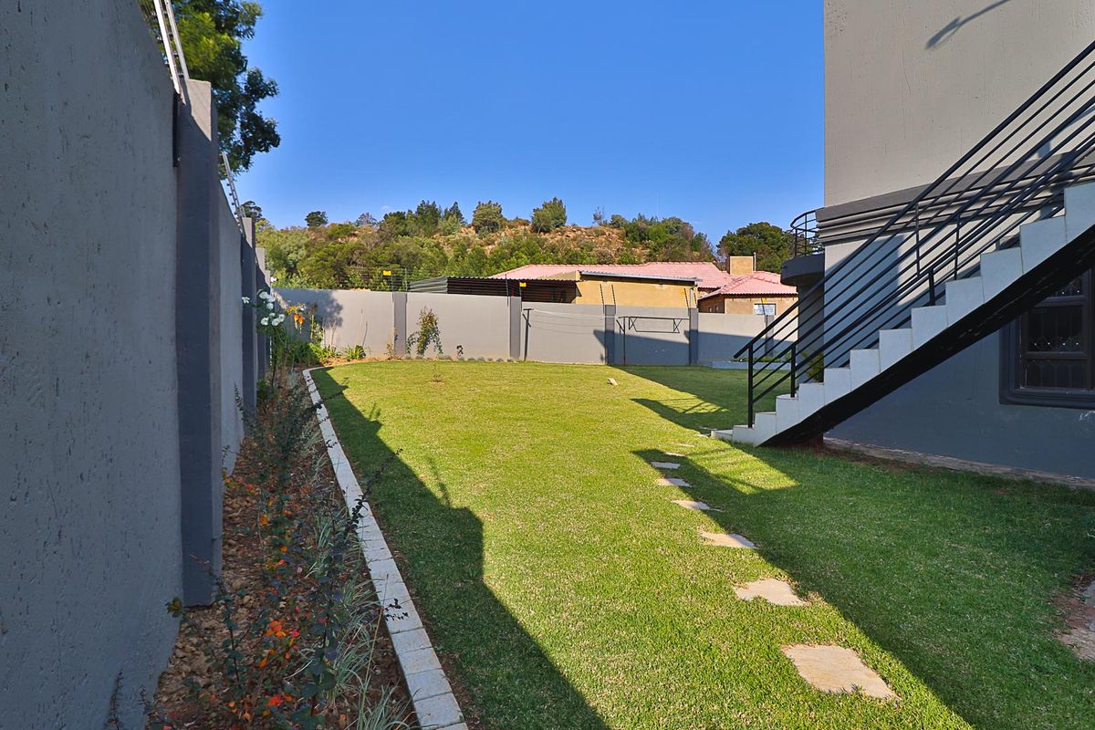 A well-maintained rear garden featuring a manicured lawn, stone pathway, perimeter wall with electric fencing, and an external staircase leading to the upper level.