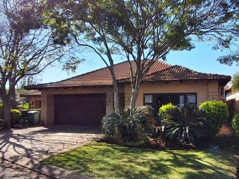 Front elevation of a single-story house featuring a tiled roof, paved driveway, and established garden landscaping.