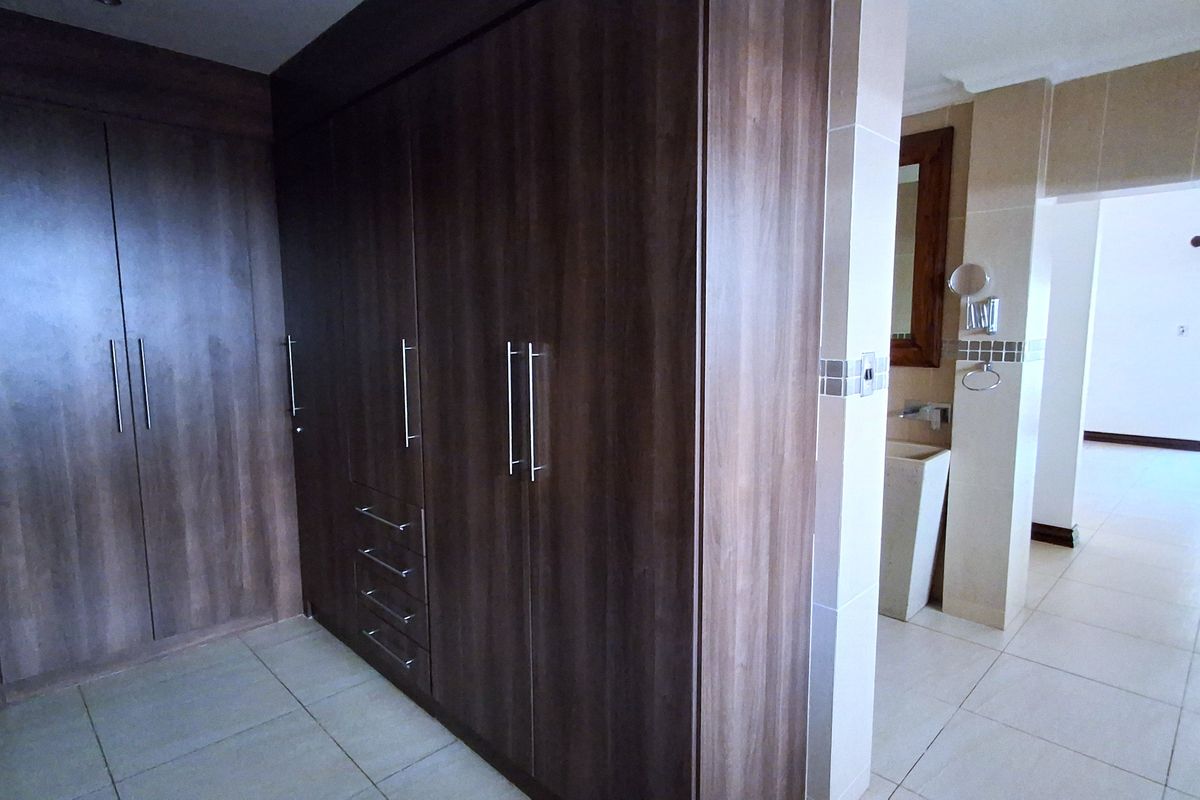 Spacious bedroom area featuring extensive built-in dark wood cabinetry and an adjoining open-plan vanity space with tiled flooring throughout.