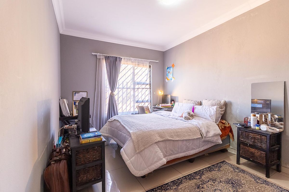 A functional bedroom featuring tiled flooring, security bars on the window, and neutral wall finishes, offering a comfortable and secure living space.