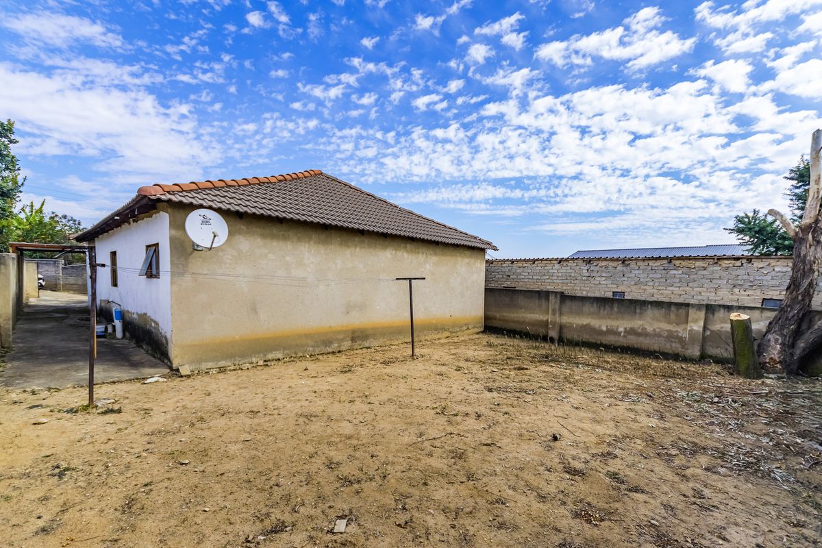 Rear view of the property showing a tiled roof, satellite dish, and a large, unlandscaped yard with perimeter walling.