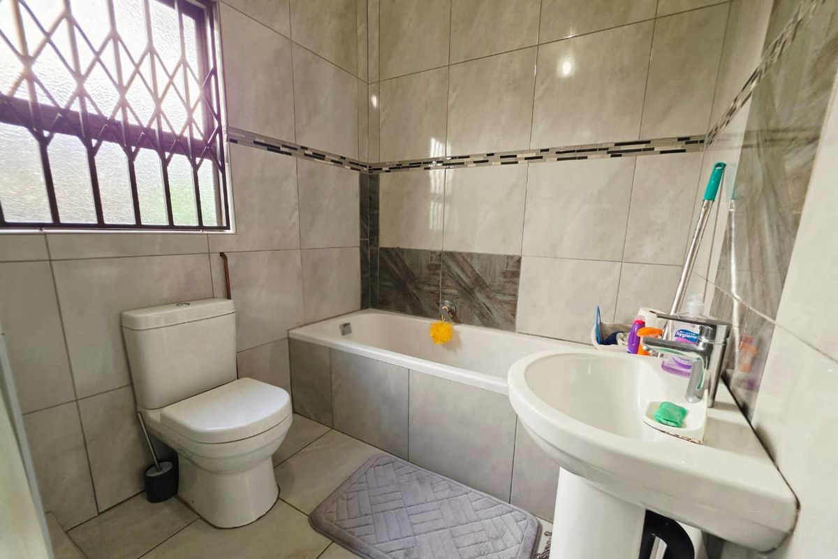 A functional bathroom featuring tiled walls, a bathtub, a pedestal basin, and a toilet, with a security gate on the window.