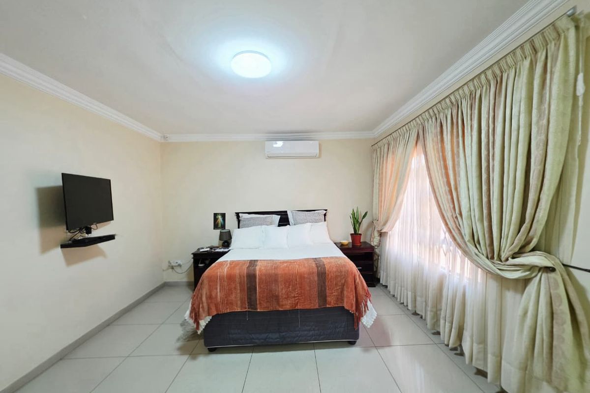 A well-maintained bedroom featuring tiled flooring, a wall-mounted television bracket, and a split-system air conditioning unit for climate control.