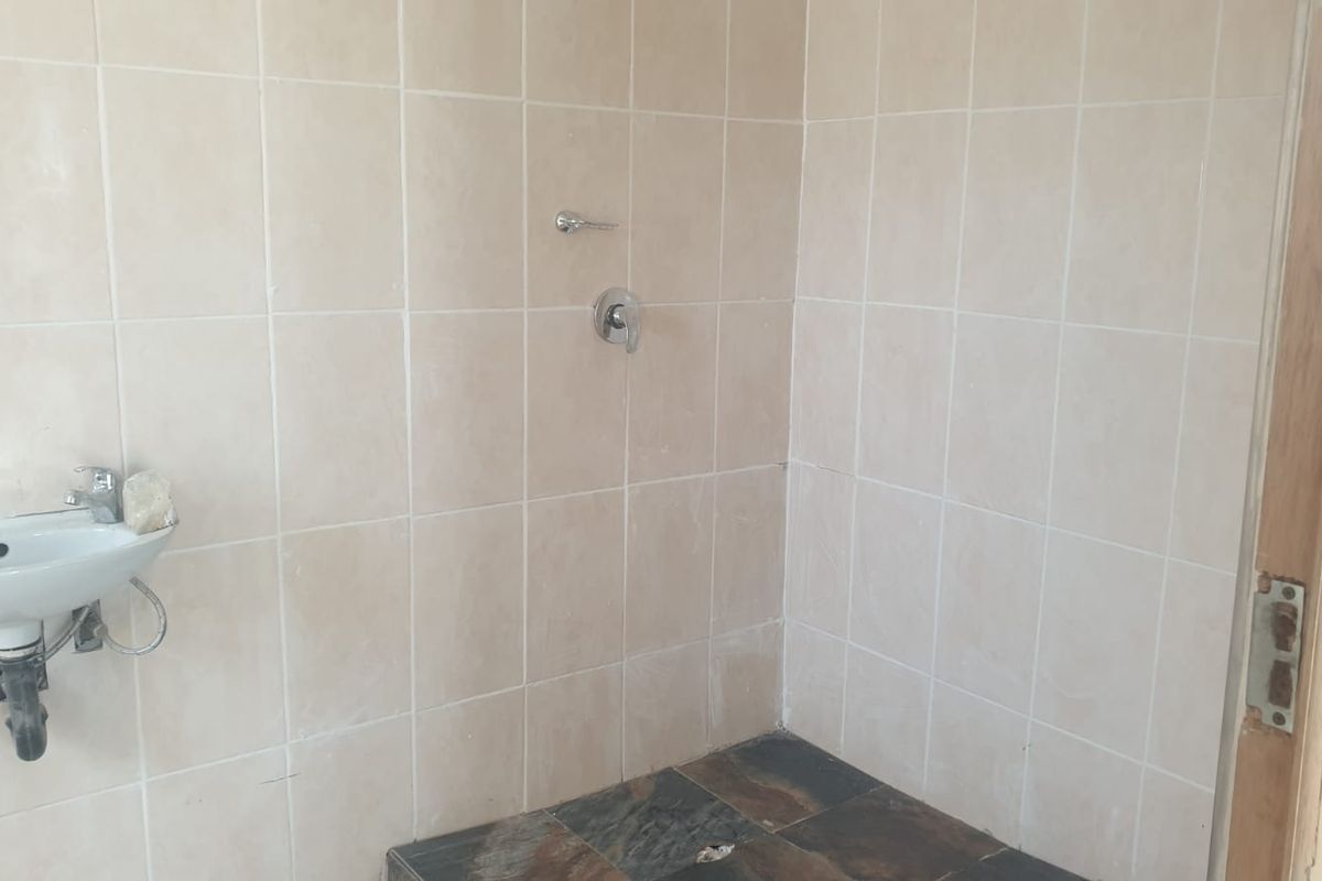 A basic bathroom featuring tiled walls, a wall-mounted basin, and a shower area with exposed plumbing fixtures.