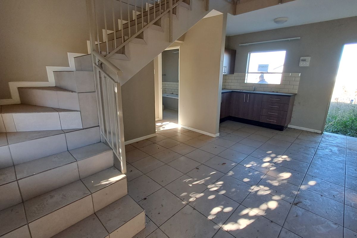 Open plan living area featuring a tiled staircase with metal balustrade and a compact kitchen with subway tile backsplash and dark cabinetry.