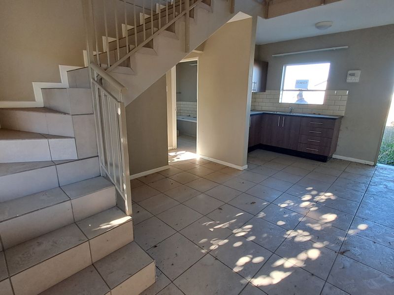 Open plan living area featuring a tiled staircase with metal balustrade and a compact kitchen with subway tile backsplash and dark cabinetry.