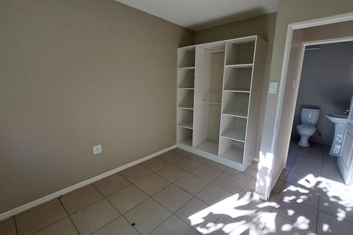 A vacant bedroom featuring neutral wall tones, tiled flooring, and an open-concept built-in shelving unit, with an adjacent bathroom visible.