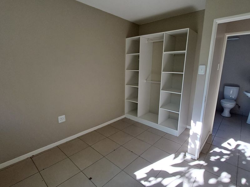 A vacant bedroom featuring neutral wall tones, tiled flooring, and an open-concept built-in shelving unit, with an adjacent bathroom visible.