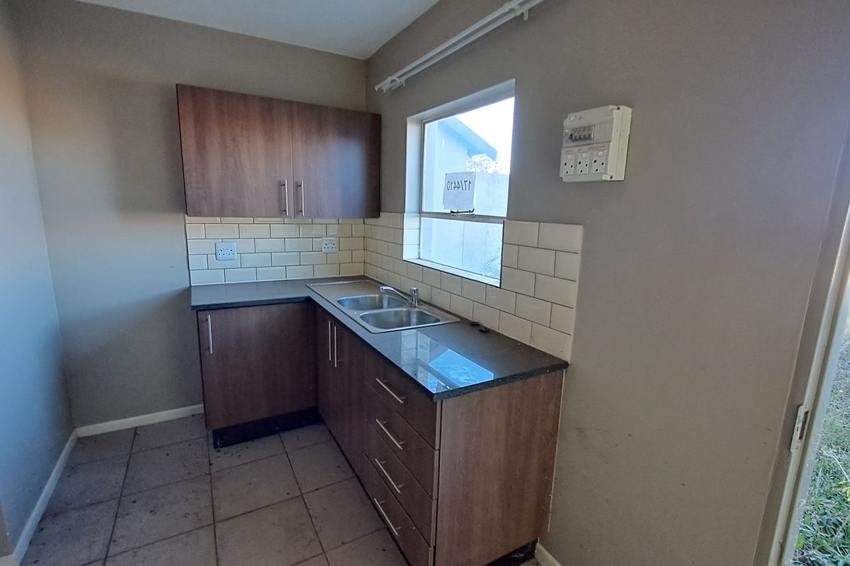 A compact kitchen featuring laminate cabinetry, a double sink, subway tile backsplash, and a functional layout, ready for personalization.