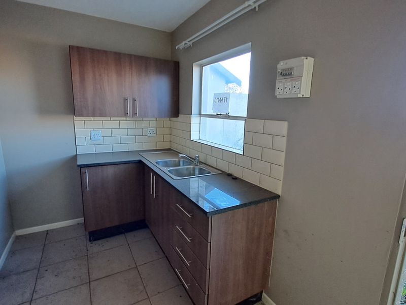 A compact kitchen featuring laminate cabinetry, a double sink, subway tile backsplash, and a functional layout, ready for personalization.