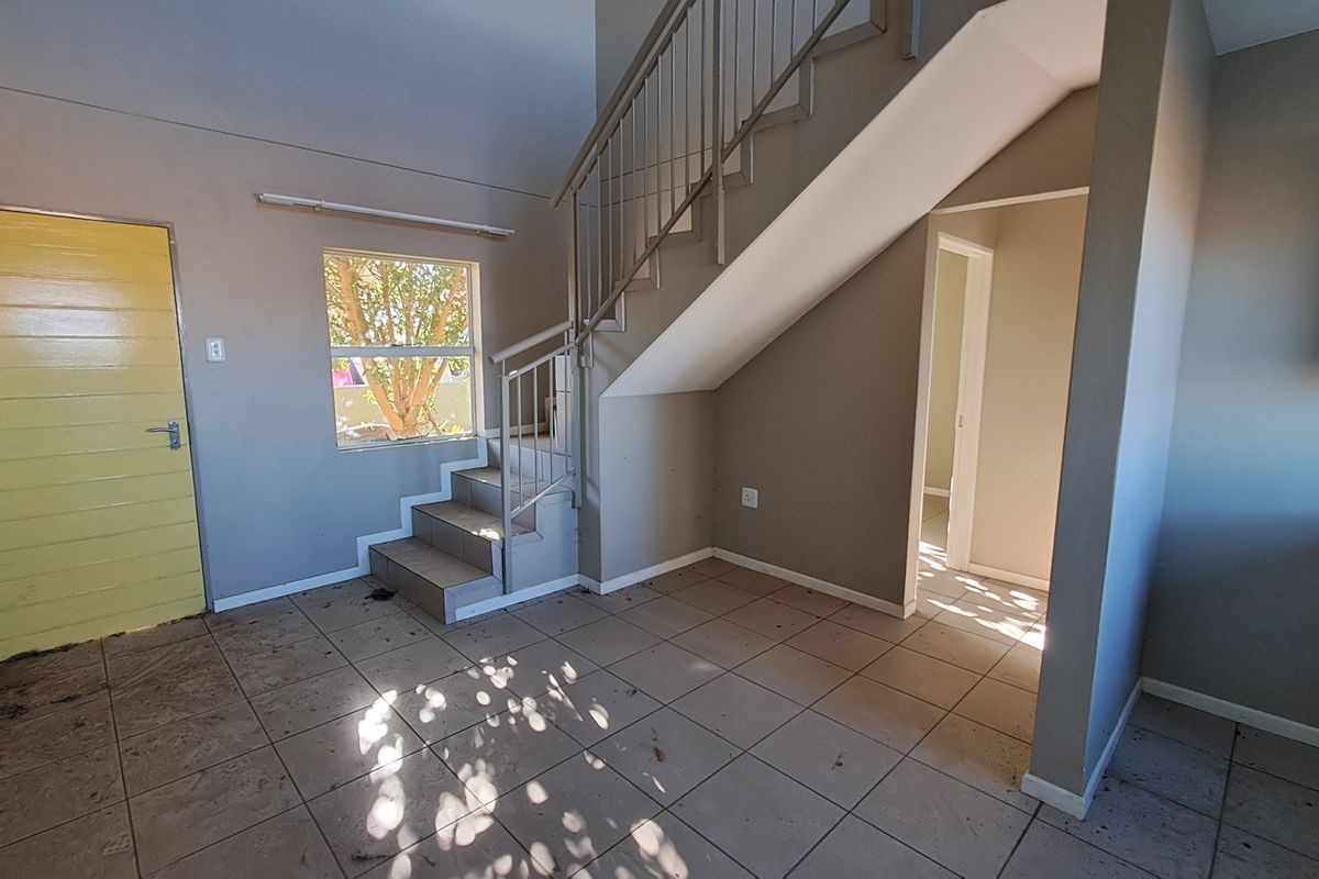 An empty living area featuring tiled flooring and a staircase with a metal railing, leading to an adjacent room.
