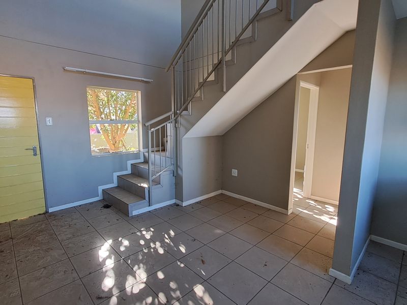An empty living area featuring tiled flooring and a staircase with a metal railing, leading to an adjacent room.