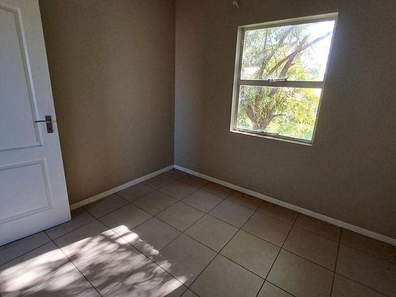 An empty bedroom featuring neutral wall paint, tiled flooring, and a window providing natural light.