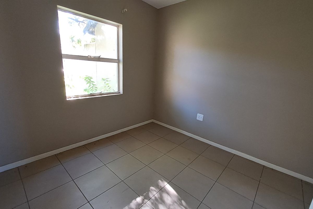 A vacant bedroom featuring neutral wall paint, tiled flooring, and a single window, providing a clean and versatile space ready for personalization.