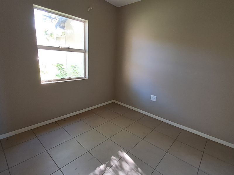 A vacant bedroom featuring neutral wall paint, tiled flooring, and a single window, providing a clean and versatile space ready for personalization.