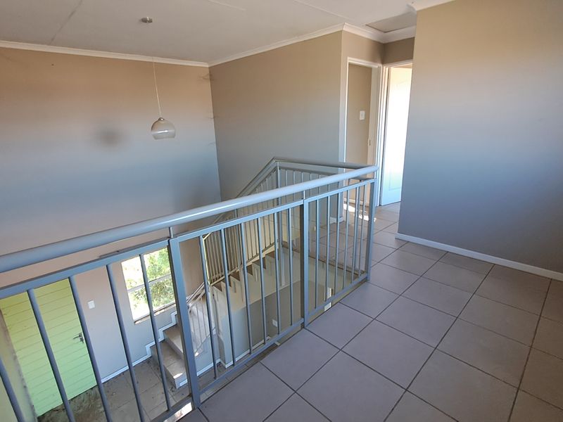 An open landing area featuring tiled flooring and a metal balustrade overlooking the staircase, providing access to adjacent rooms.