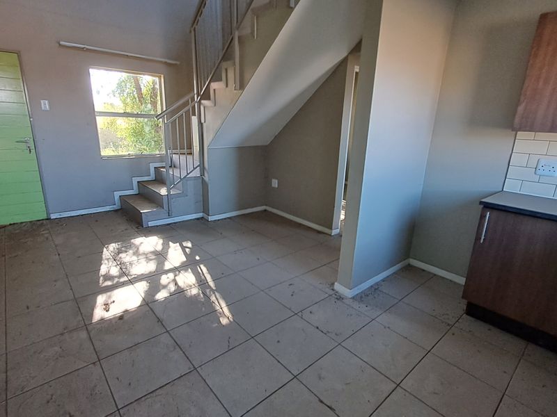 Open plan living and kitchen area featuring tiled flooring, a staircase with metal handrail, and built-in kitchen cabinetry with a subway tile backsplash.