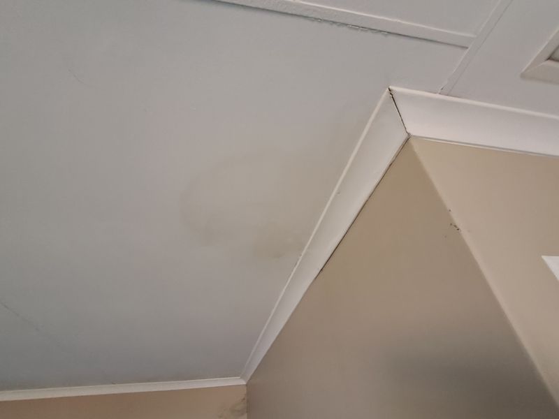 Close-up view of a ceiling corner showing visible water staining and cracked cornice joints, indicating potential maintenance requirements.