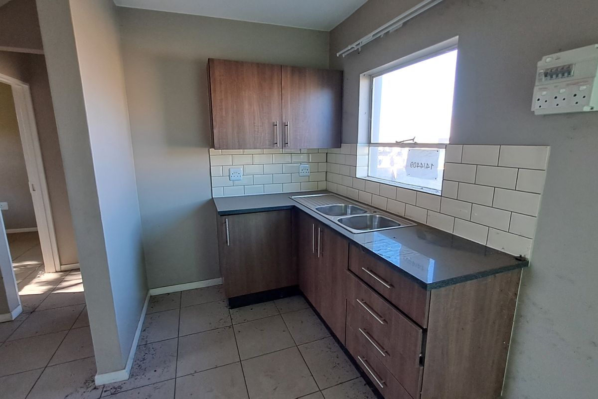 A compact kitchen featuring laminate cabinetry, subway tile backsplash, and a stainless steel sink, presenting a functional space ready for minor cosmetic updates.