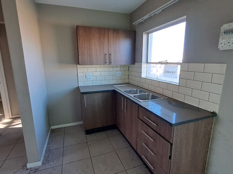 A compact kitchen featuring laminate cabinetry, subway tile backsplash, and a stainless steel sink, presenting a functional space ready for minor cosmetic updates.