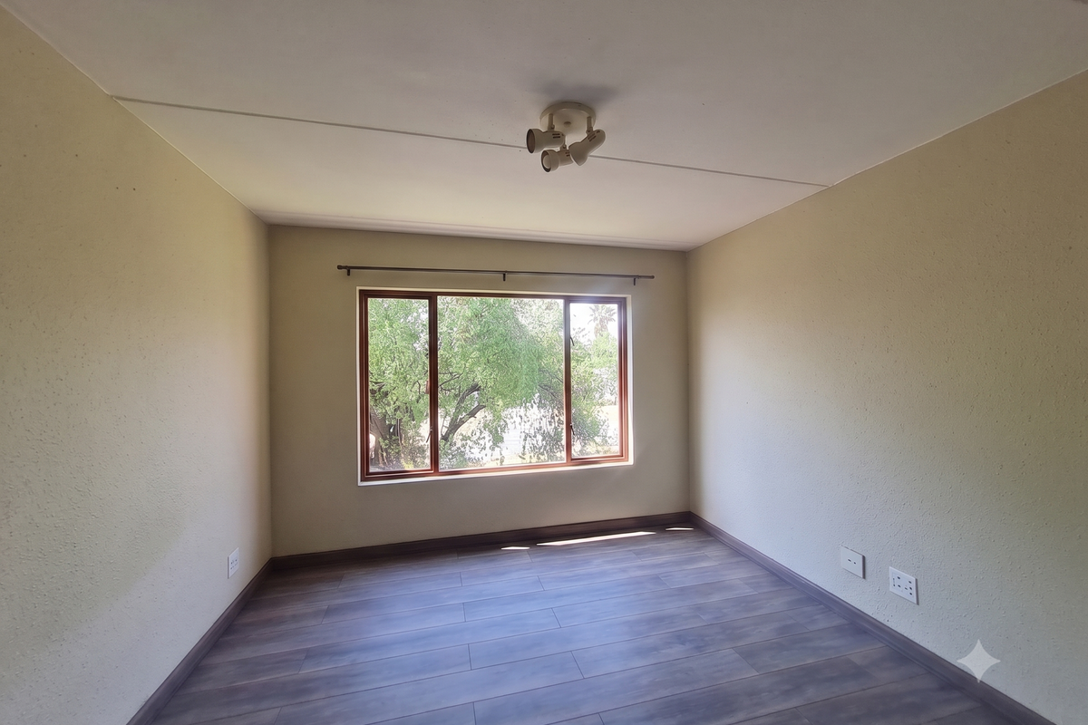 A bright, empty bedroom featuring laminate flooring, neutral walls, and a large window providing natural light and garden views.