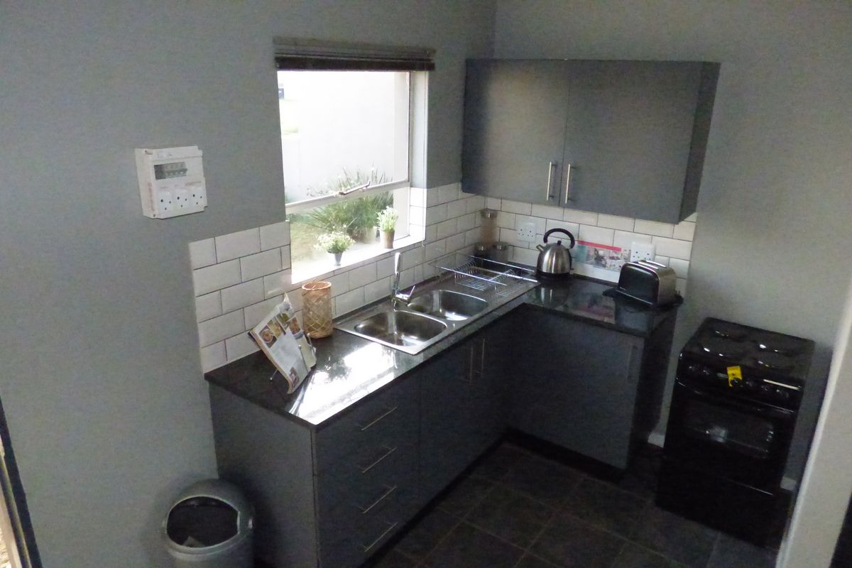 Compact kitchen featuring modern grey cabinetry, granite countertops, subway tile backsplash, and a double basin sink with a window view.