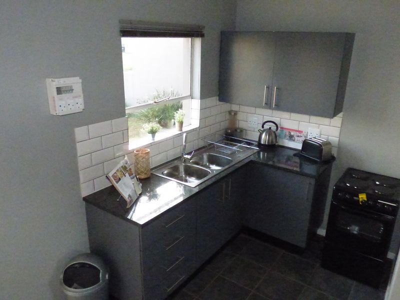Compact kitchen featuring modern grey cabinetry, granite countertops, subway tile backsplash, and a double basin sink with a window view.