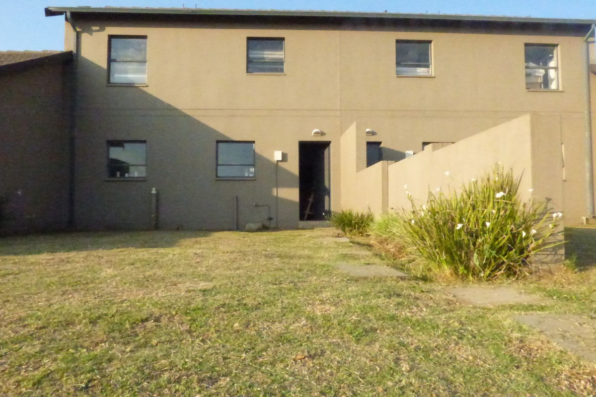 Rear view of a townhouse featuring a plastered facade, tiled roof, and a private garden area with a paved walkway.
