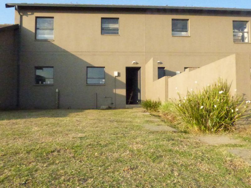 Rear view of a townhouse featuring a plastered facade, tiled roof, and a private garden area with a paved walkway.
