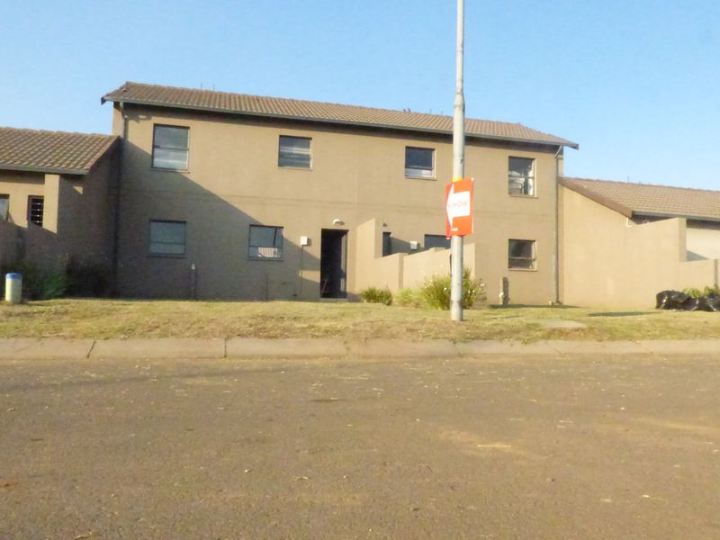 Front elevation of a two-story townhouse featuring a plastered facade, tiled roof, and paved driveway area.