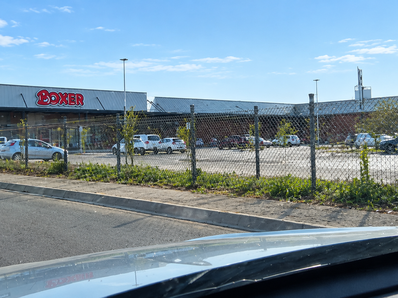 A view of a commercial retail building with a paved parking lot, enclosed by a chain-link fence.