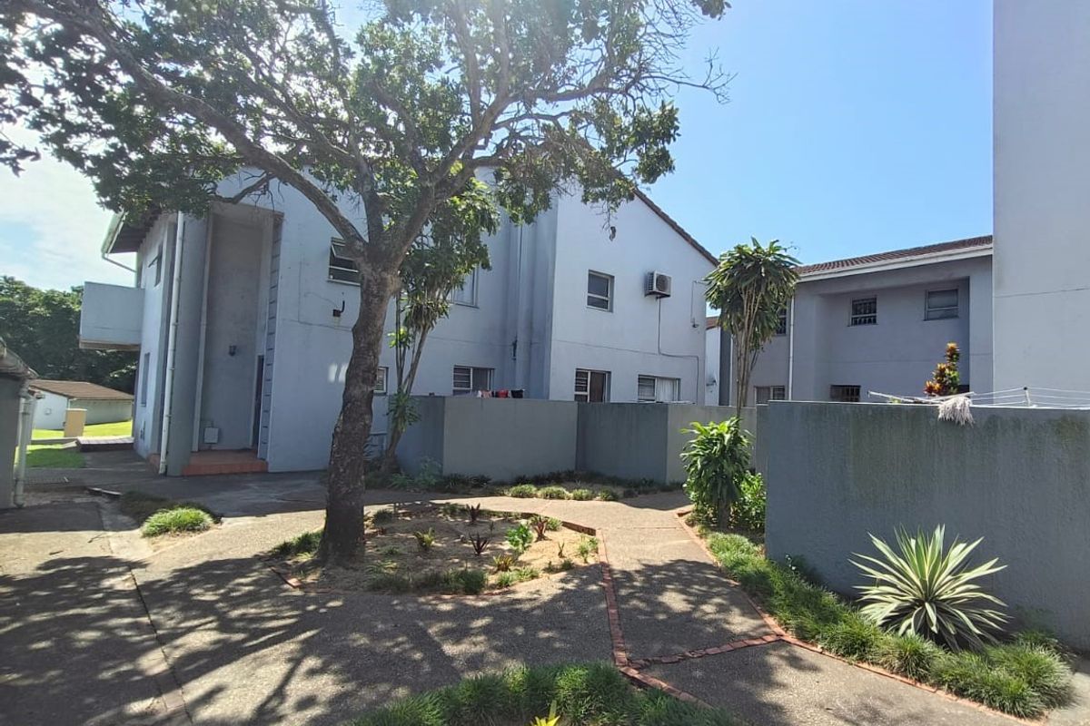 A view of the rear exterior area of the townhouse complex, featuring paved walkways, mature trees, and shared outdoor space.