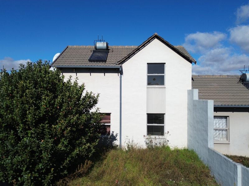 Rear view of a two-story townhouse featuring a tiled roof with solar water heating system and a private garden area.