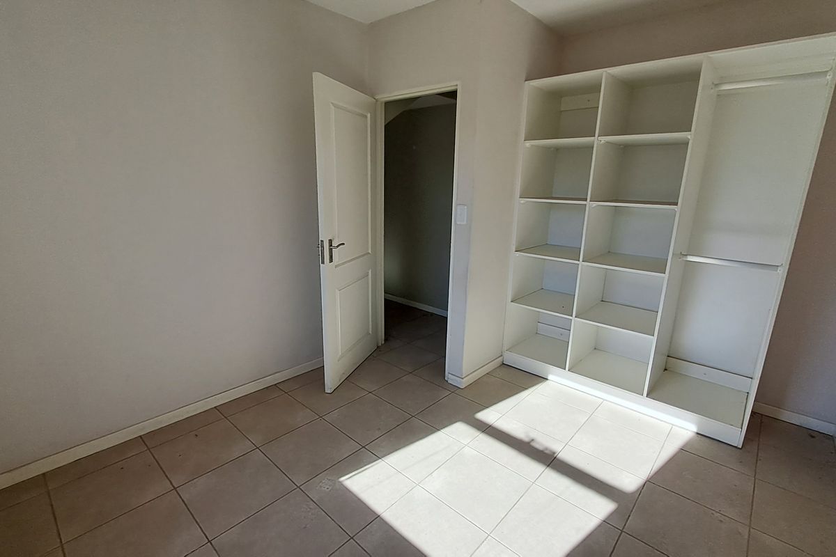 A bright, empty bedroom featuring neutral tiled flooring and built-in open shelving, offering a clean canvas for personalization.