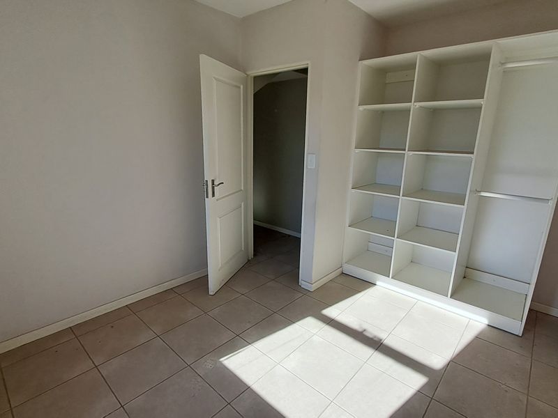 A bright, empty bedroom featuring neutral tiled flooring and built-in open shelving, offering a clean canvas for personalization.